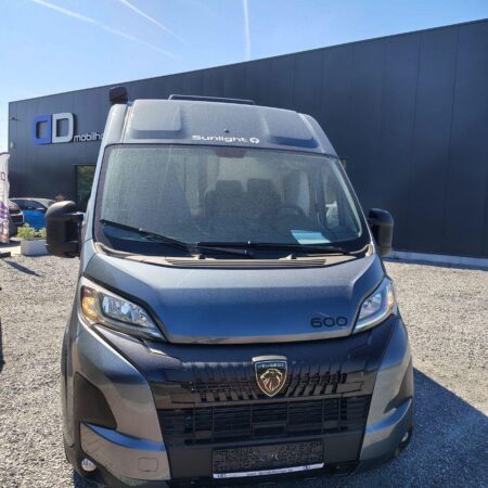 Front view of a gray Peugeot Sunlight 600 camper van facing the camera in a gravel lot near a dark dealership building.