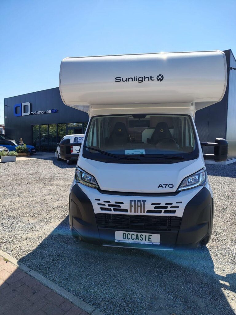 Front view of a white Fiat A70 motorhome with a large Sunlight over-cab, parked on a gravel lot at a dealership (license plate: OCCASIE)